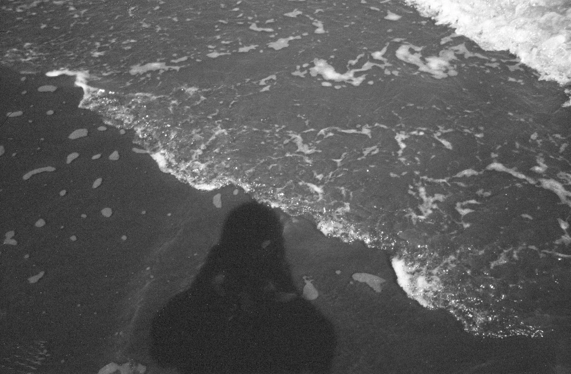 La sombra de quien toma la foto sobre la espuma de las olas, en blanco y negro.